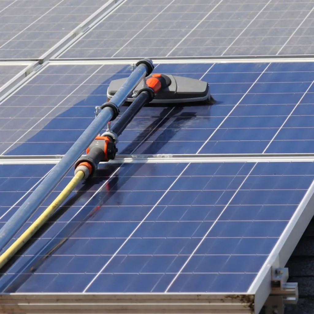 A cleaning tool with brushes and hoses is being used to clean blue solar panels on a rooftop, helping maintain their efficiency under sunlight.