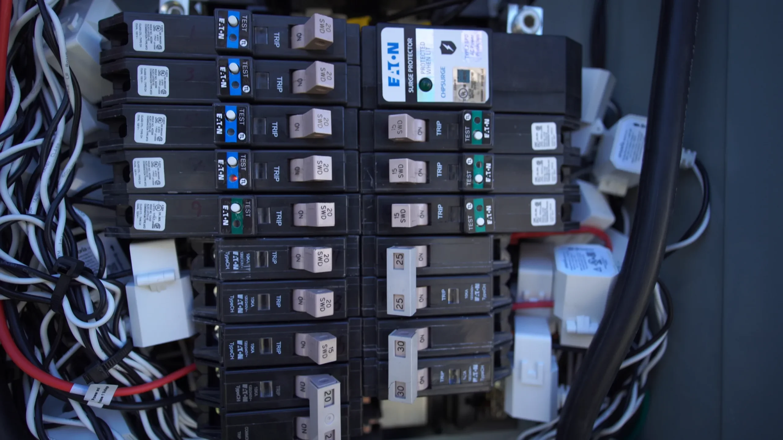 Close-up of an electrical breaker panel with multiple Eaton circuit breakers, labeled switches, and various wires connected, some red, black, and white, visible along the sides and bottom of the panel.